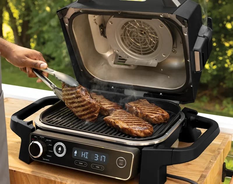 Steaks searing with grill marks on the open Ninja Woodfire grill, display reading HI