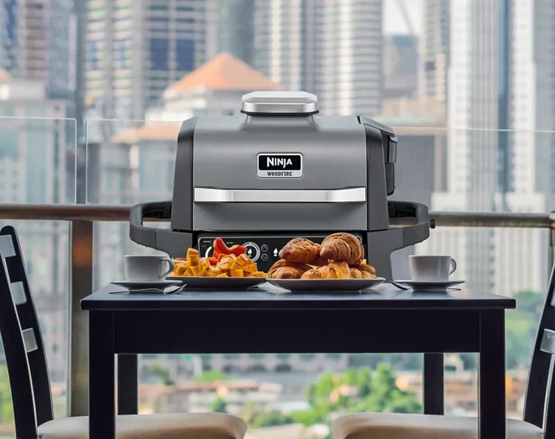 Ninja Woodfire grill on a city balcony table with breakfast plates