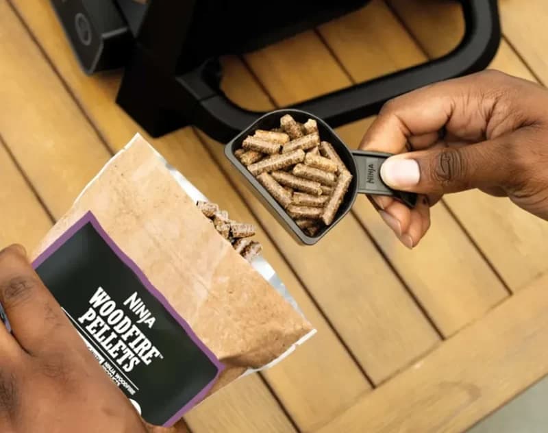 Hand scooping Ninja Woodfire Pellets from the bag into the pellet scoop