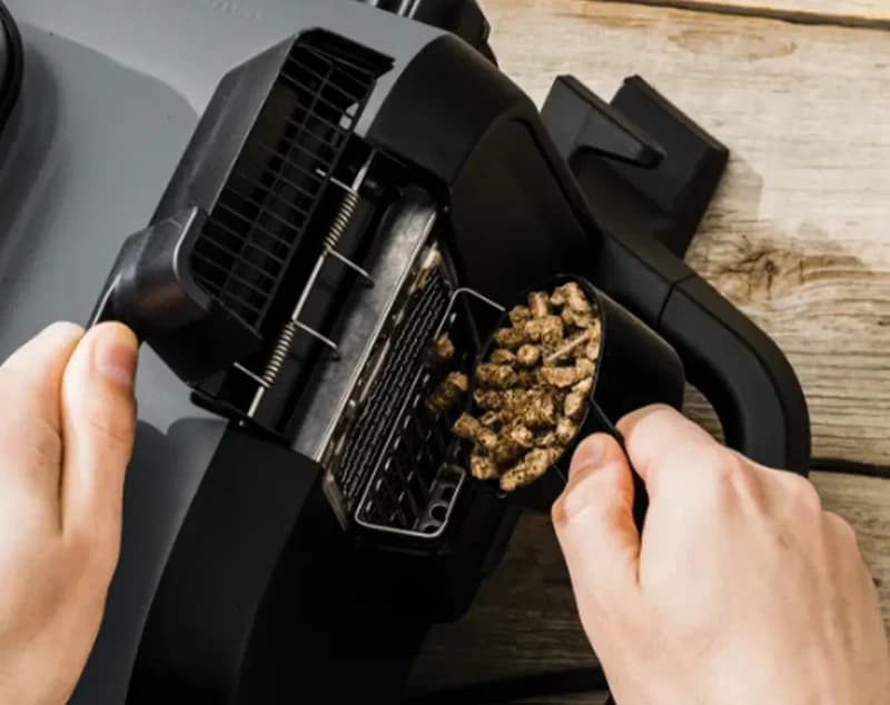 Hands loading wood pellets into the Ninja Woodfire pellet scoop