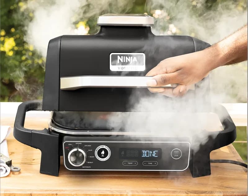 Ninja Woodfire grill releasing smoke as the lid is lifted, display reading DONE